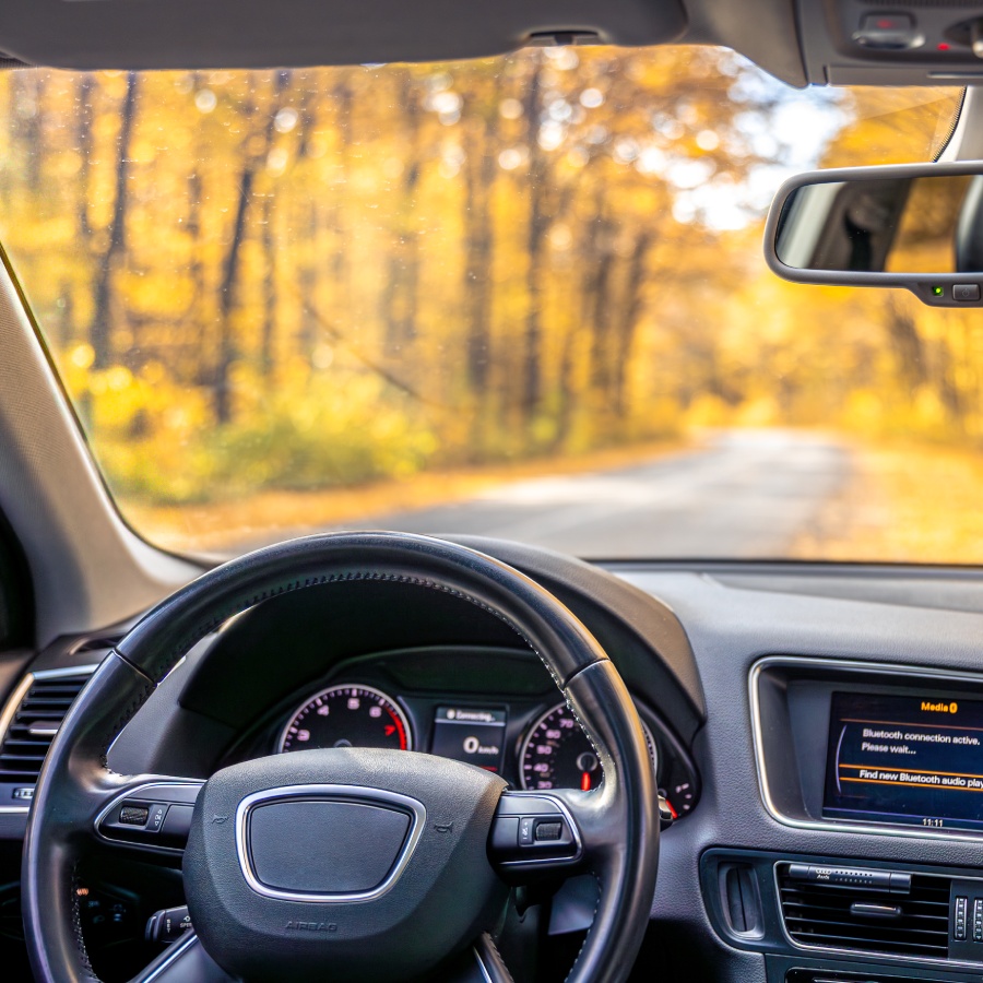 Pare-brise propre et dégagé pour une conduite sûre en automne Vue intérieure d’une voiture sur route forestière à travers un pare-brise propre et dégagé en automne.